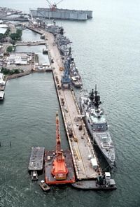 A high angle view of a floating dry dock and ships docked at the pier. The docked ships are, from front to rear, the guided missile cruiser USS WILLIAM H. STANDLEY (CG-32), the guided missile destroyer USS HENRY B. WILSON (DDG-7), the guided missile cruiser USS STERETT (CG-31) and the oiler USNS HASSAYAMPA (T-AO-145). - 1981