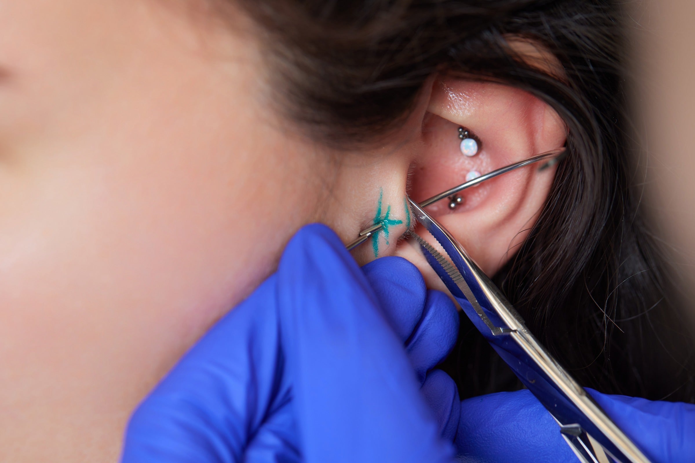 A closeup of a professional piercer performing an earlobe piercing, highlighting the use of sterilized equipment and precise technique.