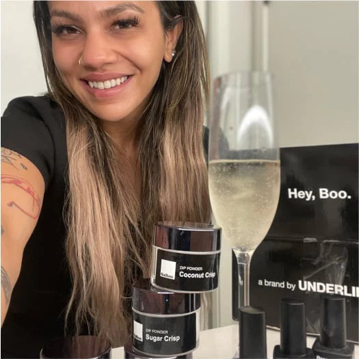 Smiling person with beauty products and a glass of sparkling wine.