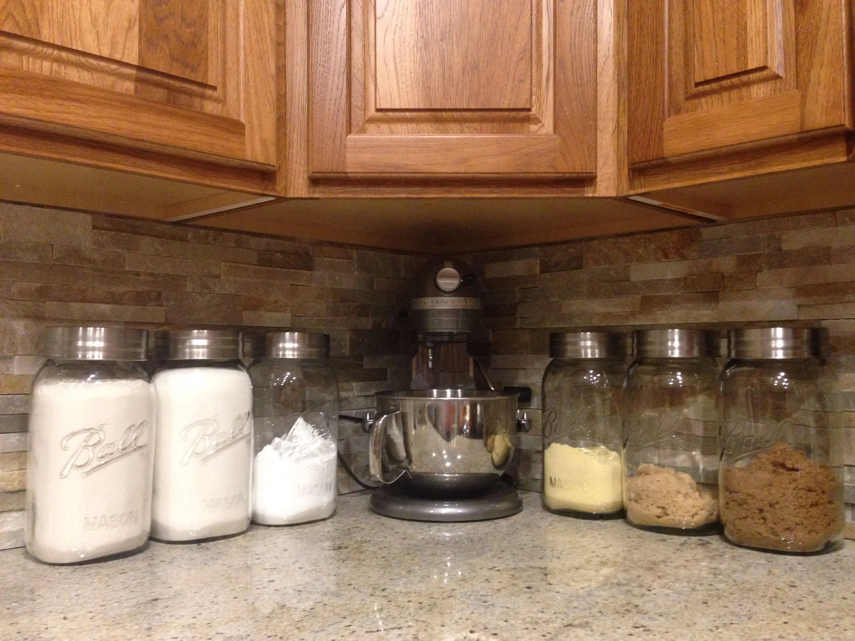 A kitchen countertop with labeled jars containing baking ingredients and a stand mixer.
