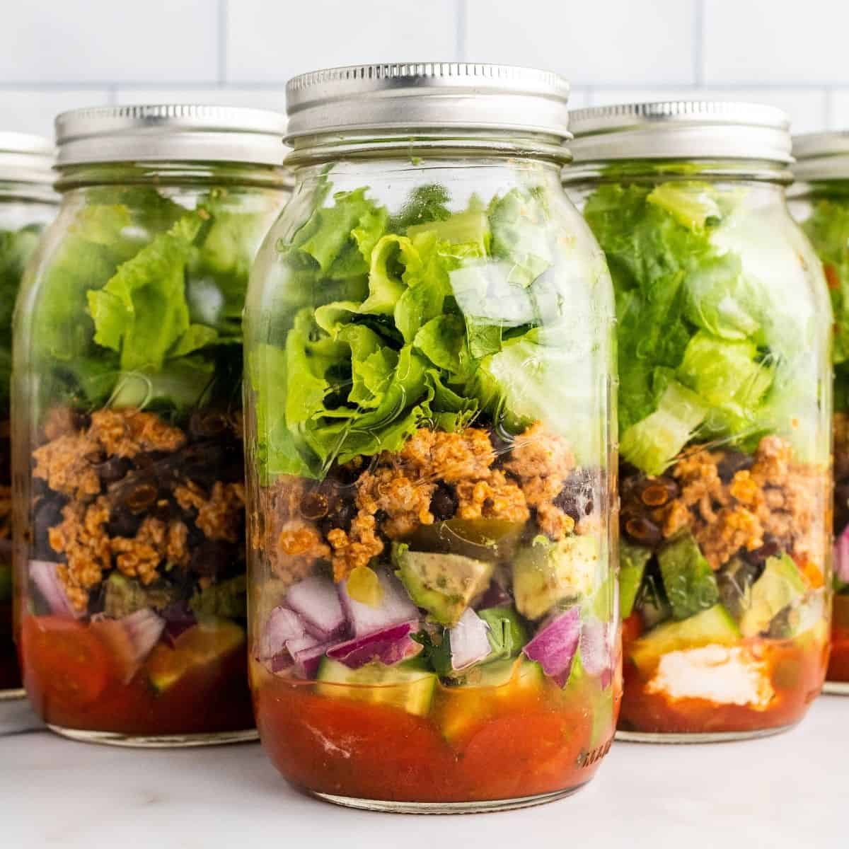 Three mason jars filled with layered taco salad ingredients.