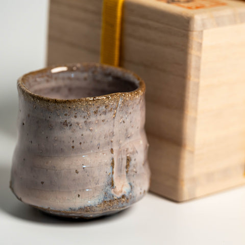 A pink Hagi yaki sake cup next to its wooden box on a white background