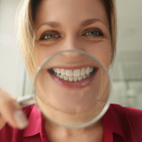 Picture of smiling woman with magnifying glass in front of mouth. For dental scaler blog post - Oral Refresh from WhiteWaveSmile