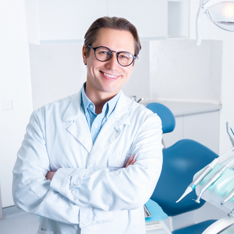 Smiling dentist with arms crossed standing in front of dental chair