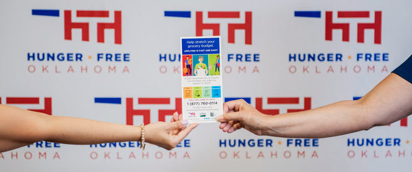 Two people's hands holding a SNAP outreach rack card in front of a Hunger Free Oklahoma background. 