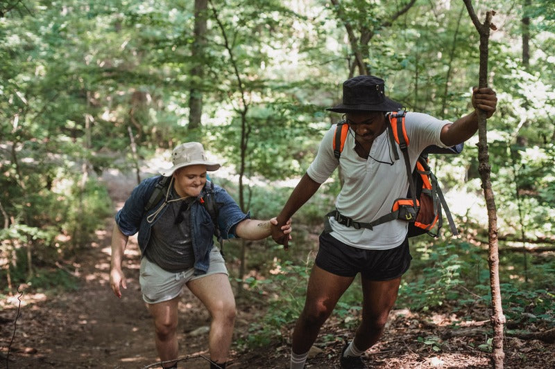 zwei Freunde wandern mit Bucket Hats durch einen Wald