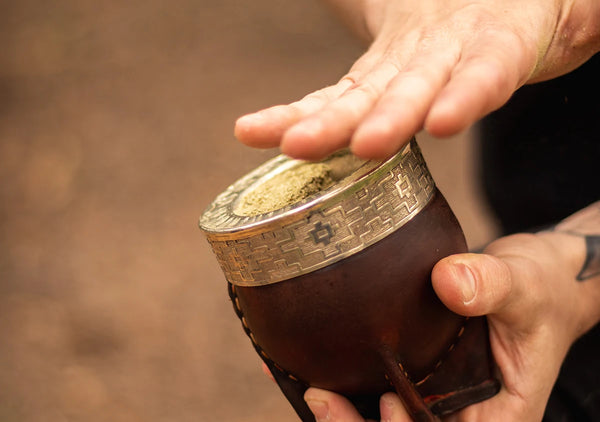 Manos de una persona preparando la yerba mate dentro del mate