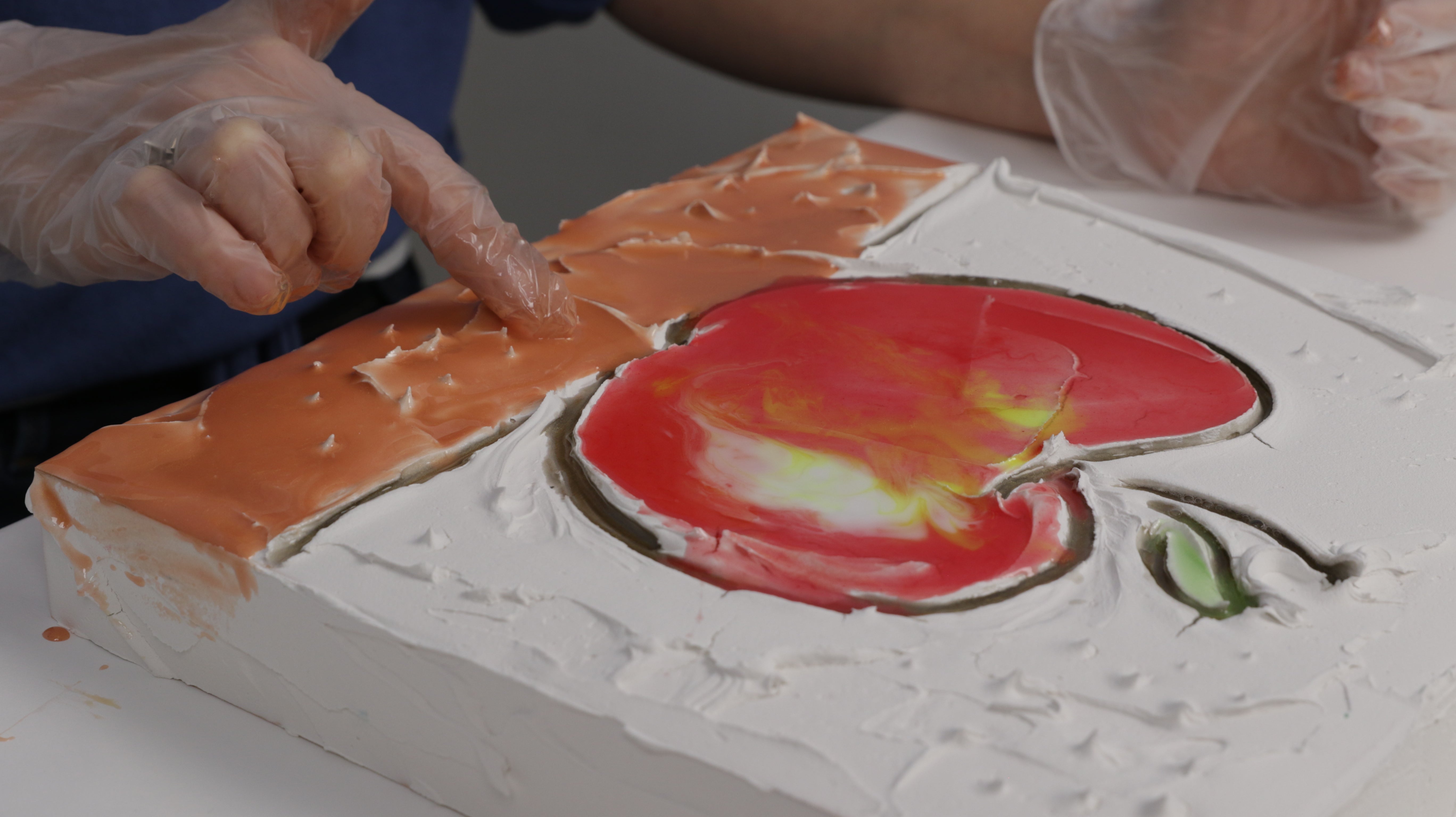 pour tinted resin over artwork using gloved hand to blend