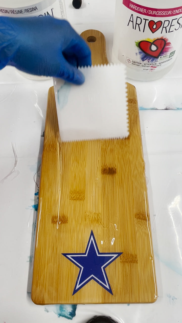 use speader tool to guide epoxy resin evenly over surface of wood board