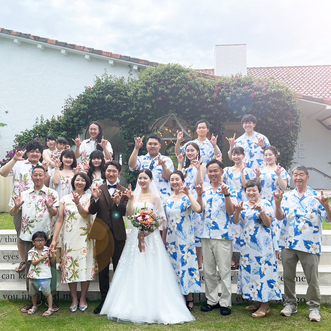 沖縄やハワイのリゾートウェディングで、新郎新婦を囲む親族とゲストがアロハシャツやムームー、かりゆしウェア姿で集合写真を撮影。南国らしい雰囲気のガーデンチャペル前で、笑顔とお揃いコーデが映える結婚式のシーン。