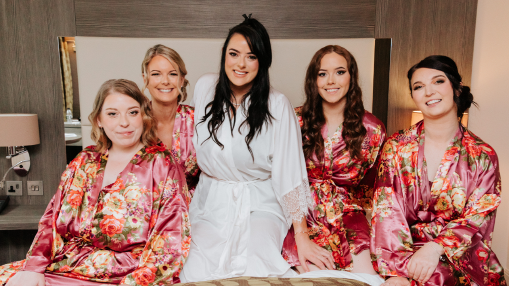 A photograph of my bridesmaids – my two sisters, Jaelithe and Hannah; my cousin, Pamela; and my sister-in-law, Claire. I insisted on these matching dressing gowns and a posed “getting ready” photo. My older sister, Jae, as you can see on the left, was less than thrilled.
