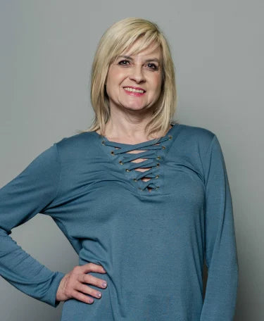 Person smiling and posing in a teal top against a gray background.