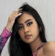 A person with long dark hair and a patterned top poses thoughtfully, touching their hair.