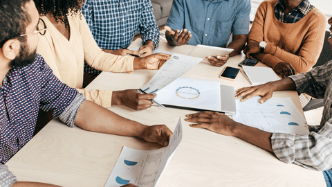 Team of creative professionals engaged in a strategic planning session with analytics reports on a wooden table, highlighting collaboration and diversity in a modern Miami workspace for a content marketing agency.