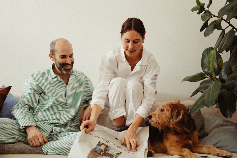couple with dog sitting on sofa, reading newspaper