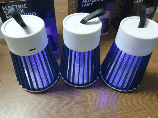 Three electric mosquito lamps with blue light on a wooden surface.