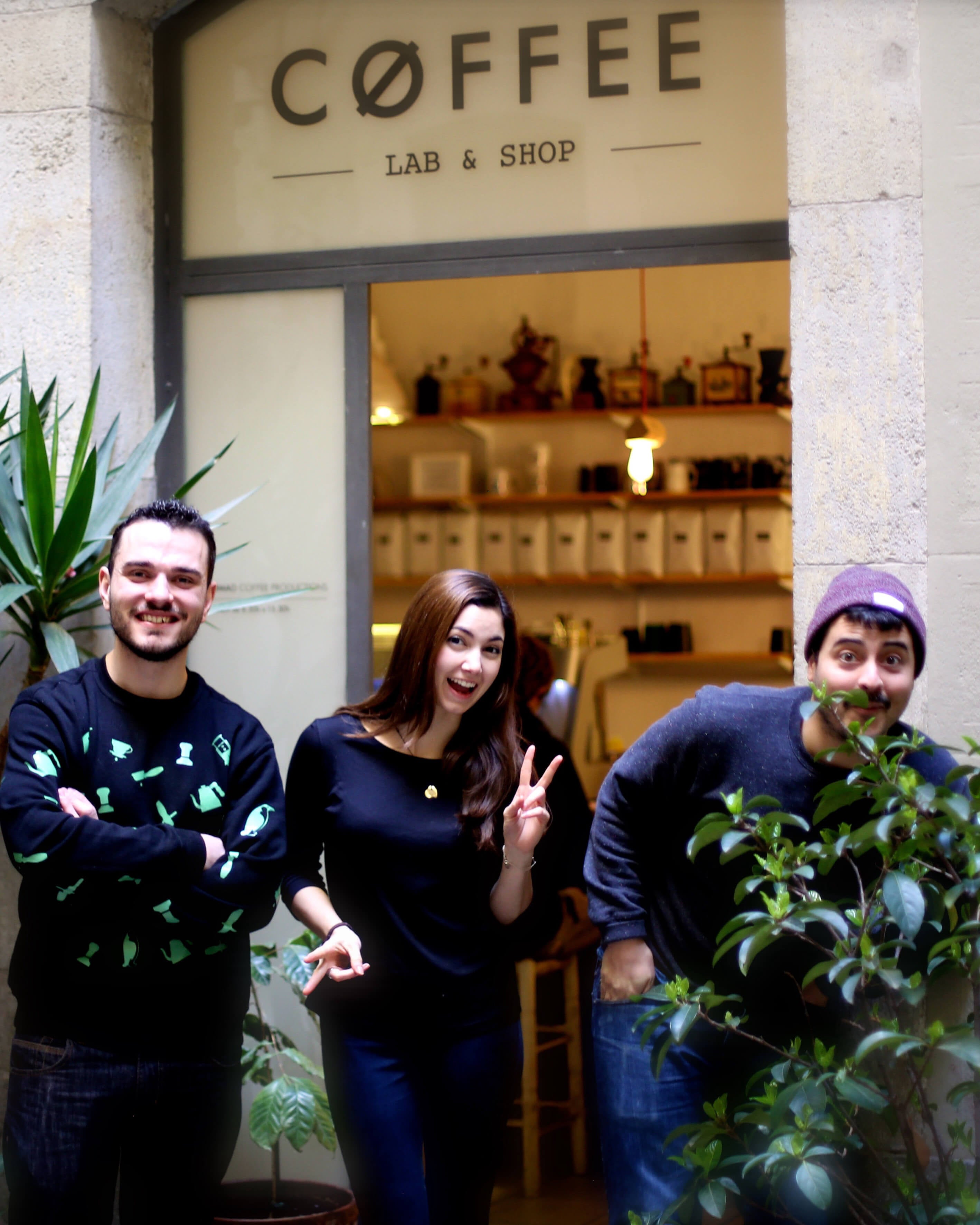 In front of the portal of Nomad Coffee Lab & Shop appear, from left to right: Fran Gonzalez, Monica Mc Coy and Jordi Mestre laughing next to some plants.