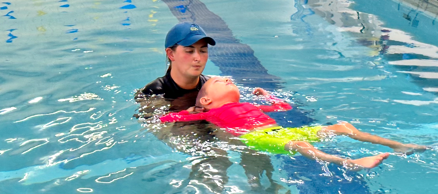 Boy floats in neon rash guard and neon board shorts during ISR survival swim lessons