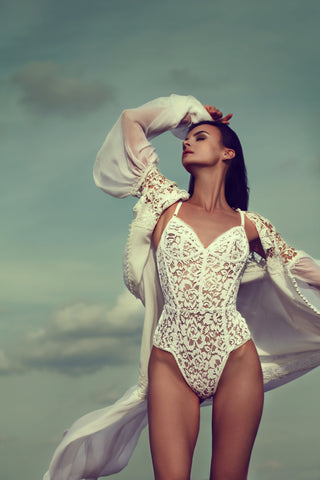 Beautiful young female wearing white lace leotard and long blouse, is enjoying light breeze from the sea.