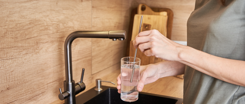 woman holding a glass of water with stainless straw in the sink