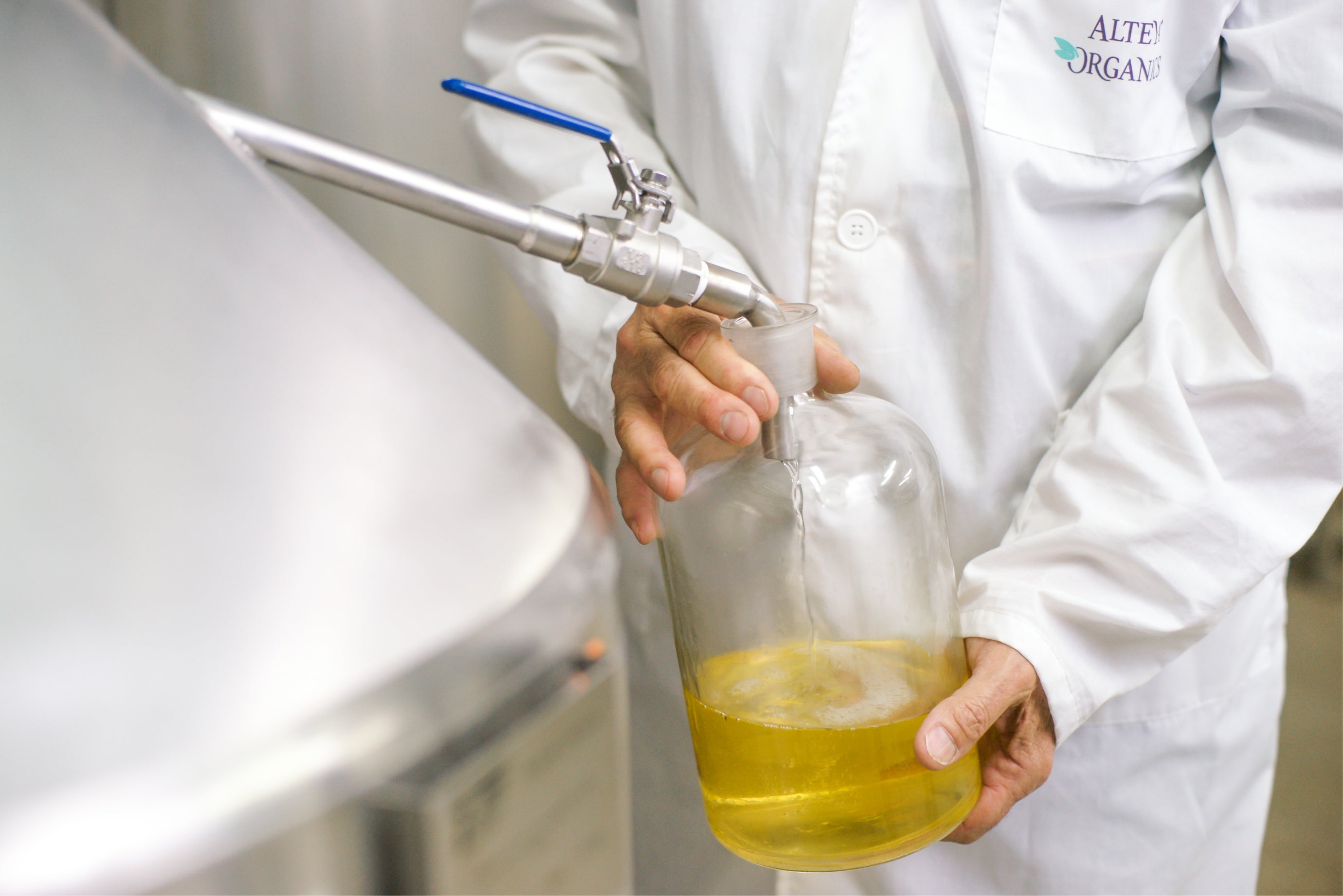 a man holding a glass bottle, pouring rose oil - rose oil distillation proccess. 