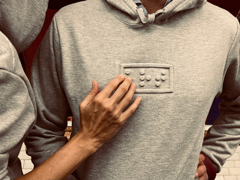 personne touchant le mot art embossé en braille sur le hoodie que porte un déficient visuel