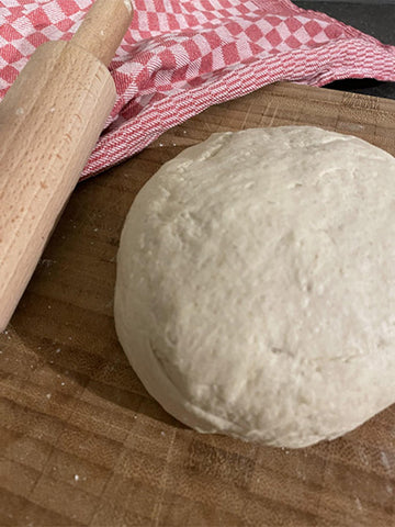 frisch hergestellter Pizzateig, der zum Ruhen auf einem Holzbrett liegt.