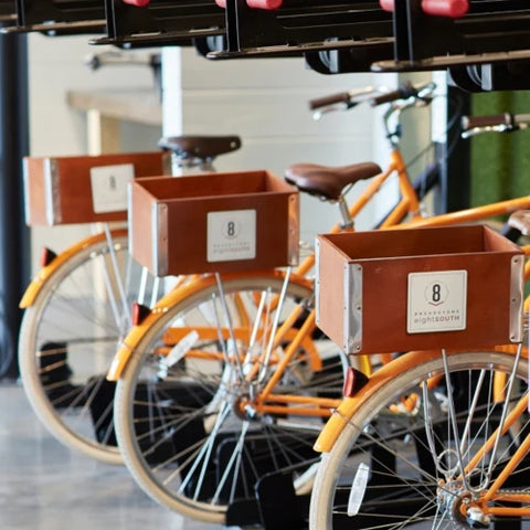 Three orange bikes in a row with wooden rear crate on carriers