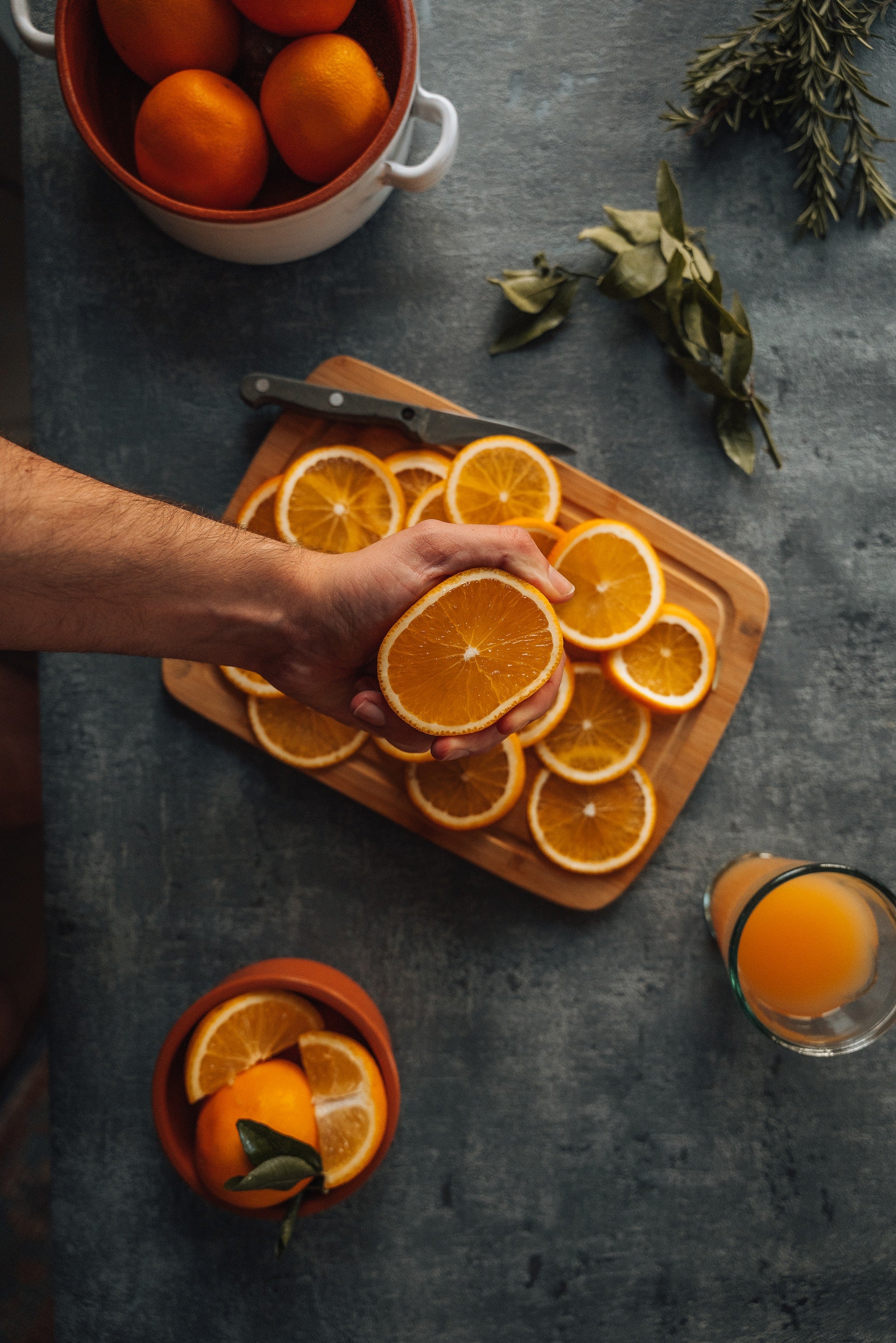 An overhead picture of a person's hand squeezing a orange above sliced oranges on a cutting board.