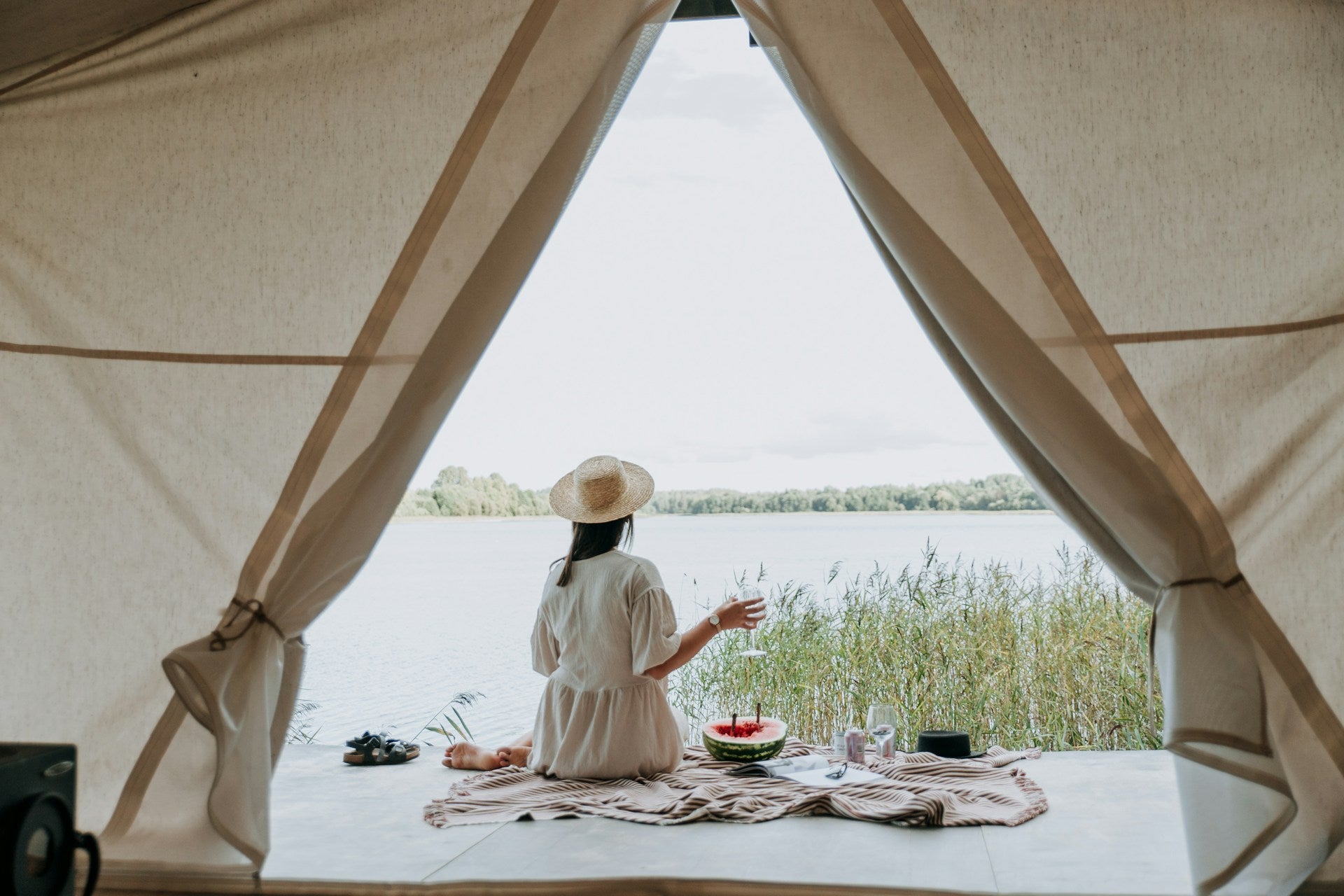 A photo taken from inside a glamping tent framing a woman wearing a white dress sitting on the porch having a delicious meal