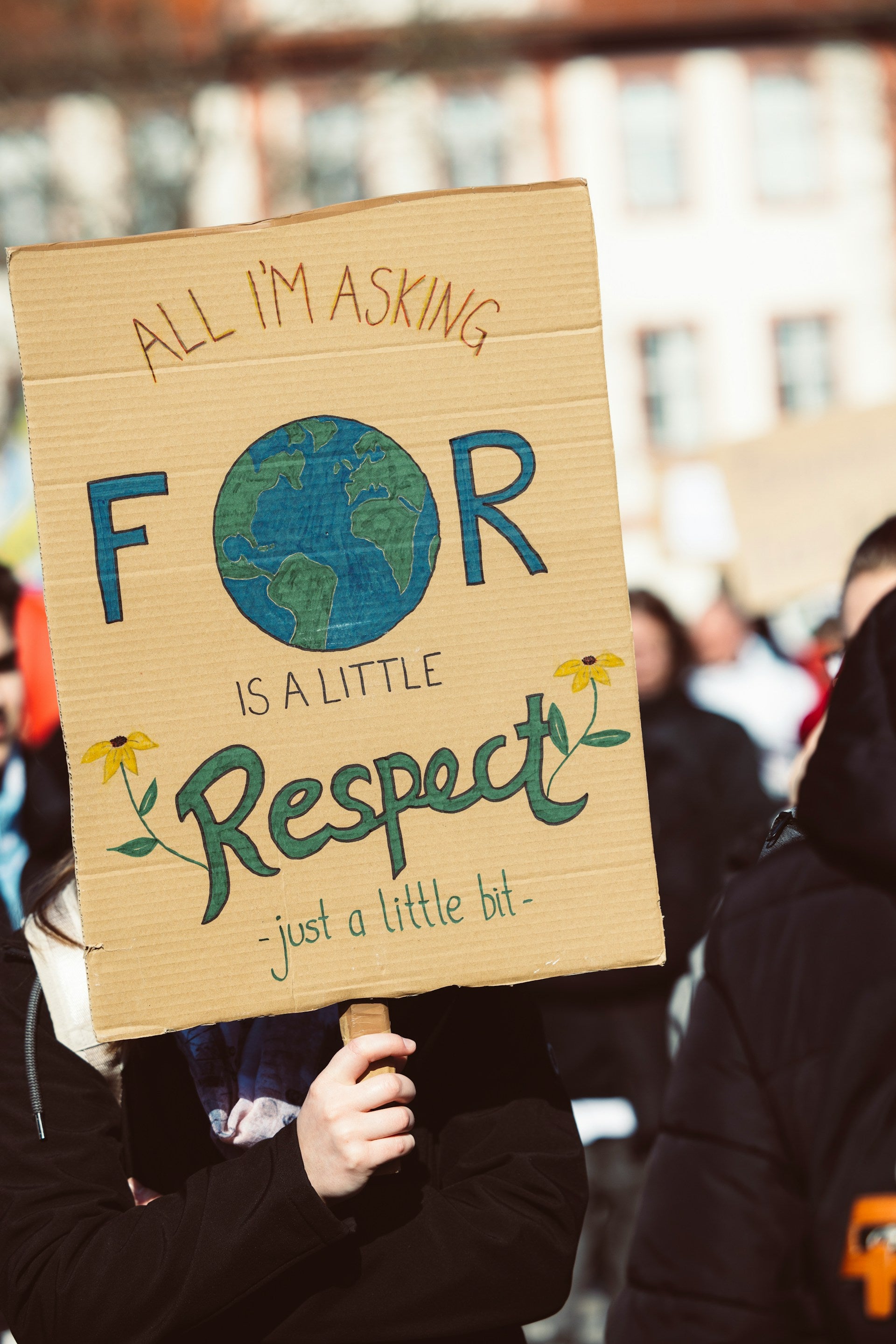 A climate activist with a poster that says "All I'm asking for is a little respect" with the planet hand-drawn on the cardboard