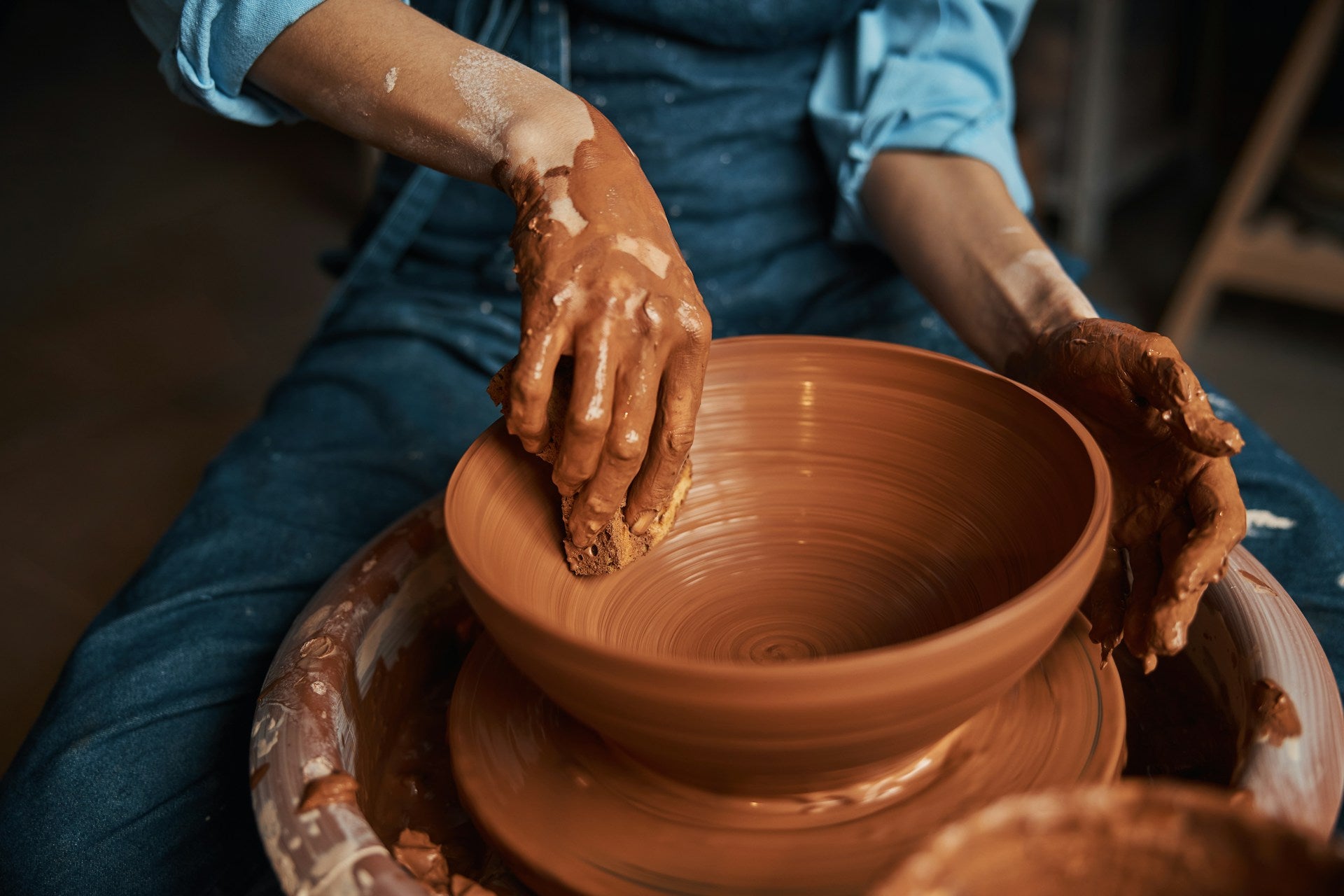 A person using a ceramics wheel to create a terra cotta bowl