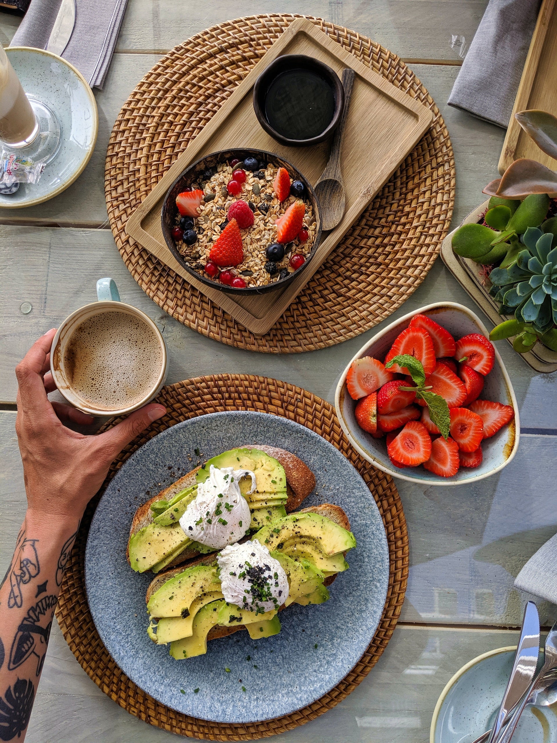 An aerial image of a food spread including avocado toast, a bowl of berries, oatmeal with berries on top, and a cup of coffee