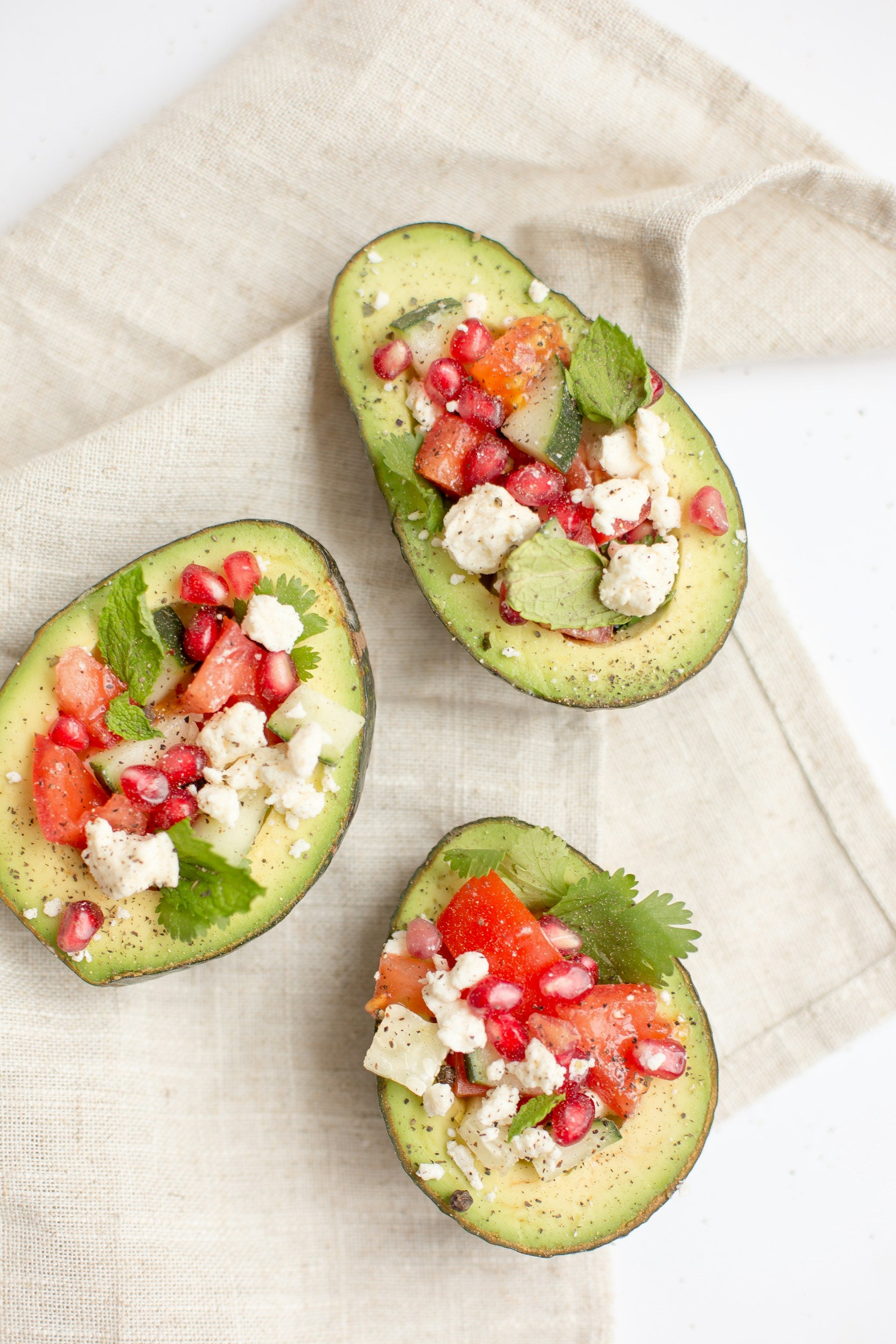 An image of three avocado halves filled with tomatoes, feta, and herbs