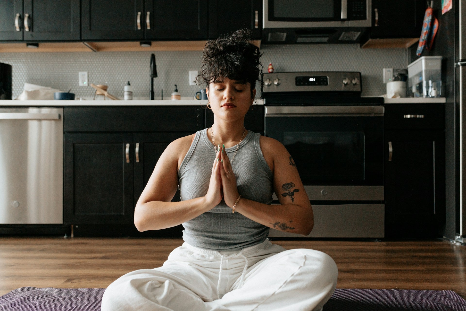 A dark-haired woman practicing meditation on a yoga mat on her kitchen floor