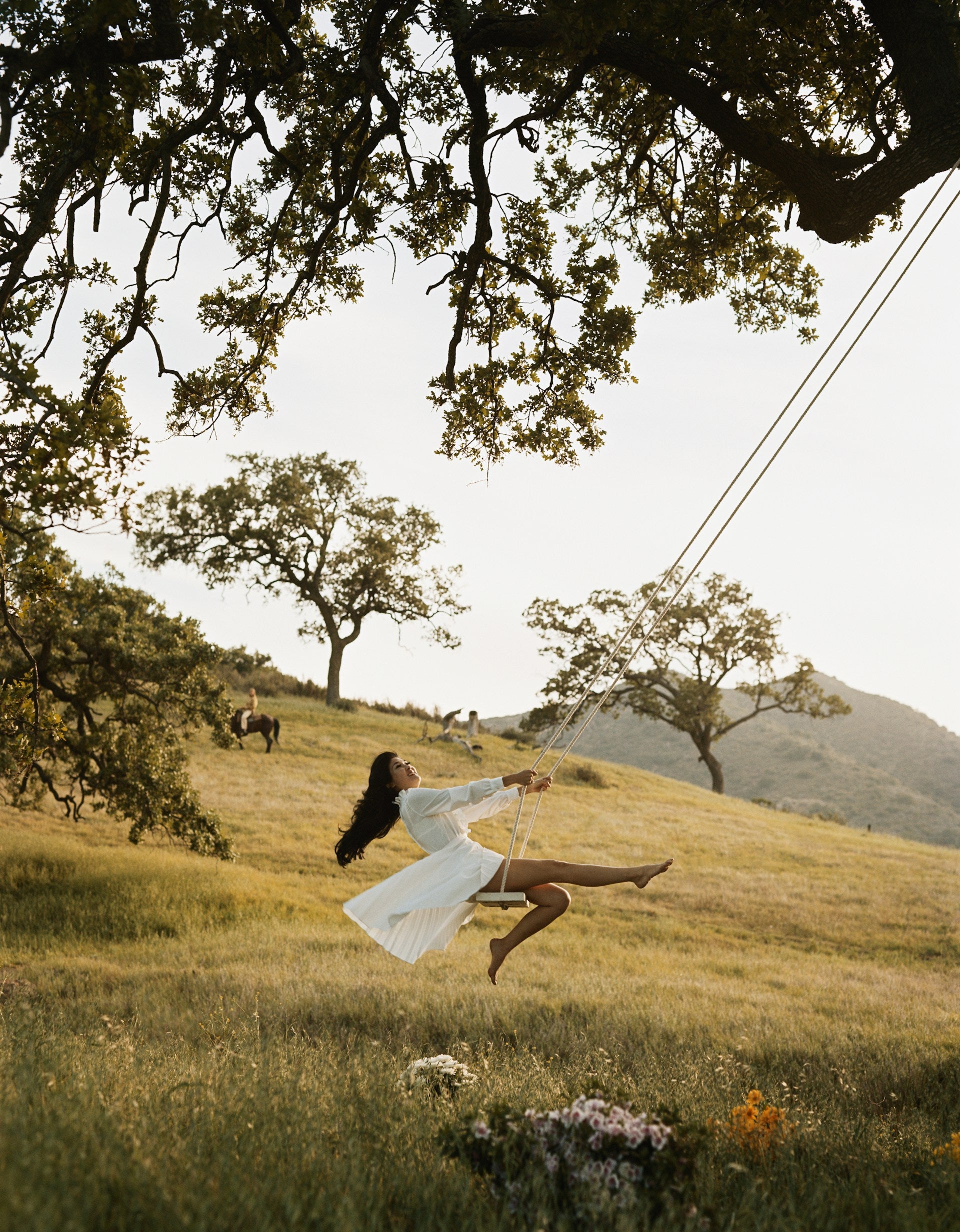 A smiling young woman in a white dress on a swing outside