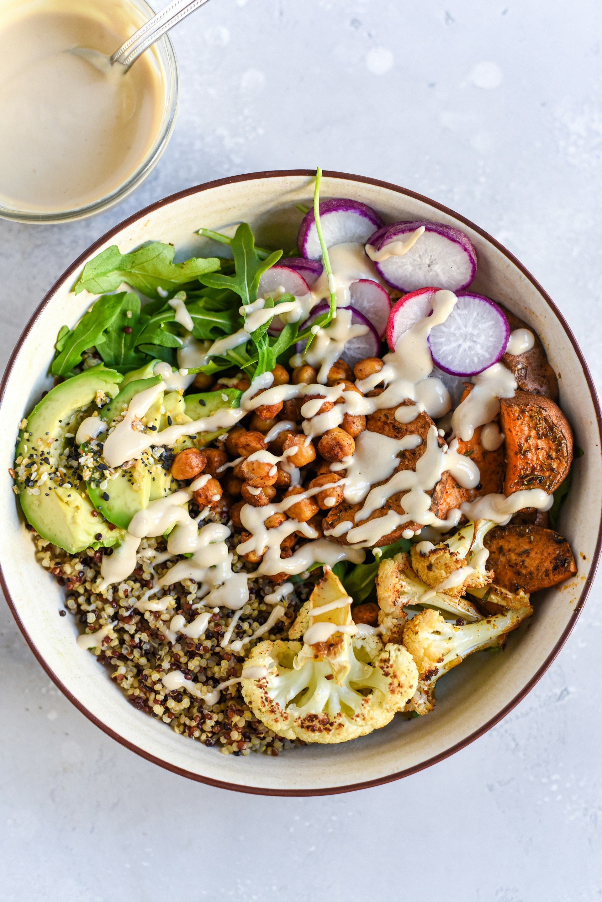 A delicious-looking, nutrient-dense nourish bowl packed with avocado, cauliflower, quinoa, radishes, cilantro, sweet potatoes, and more