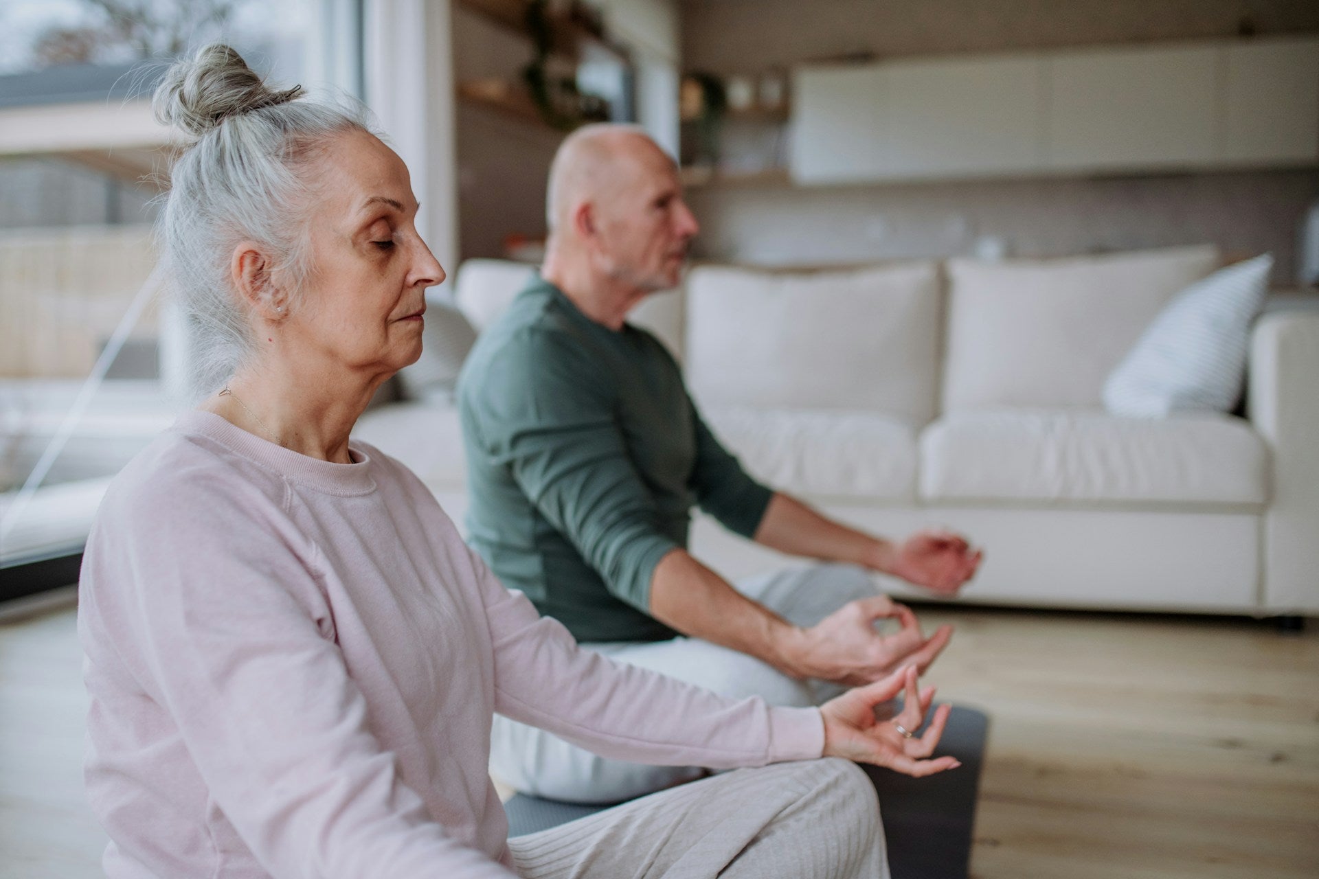 A senior couple meditating with their eyes closed, sitting crosslegged in their living room