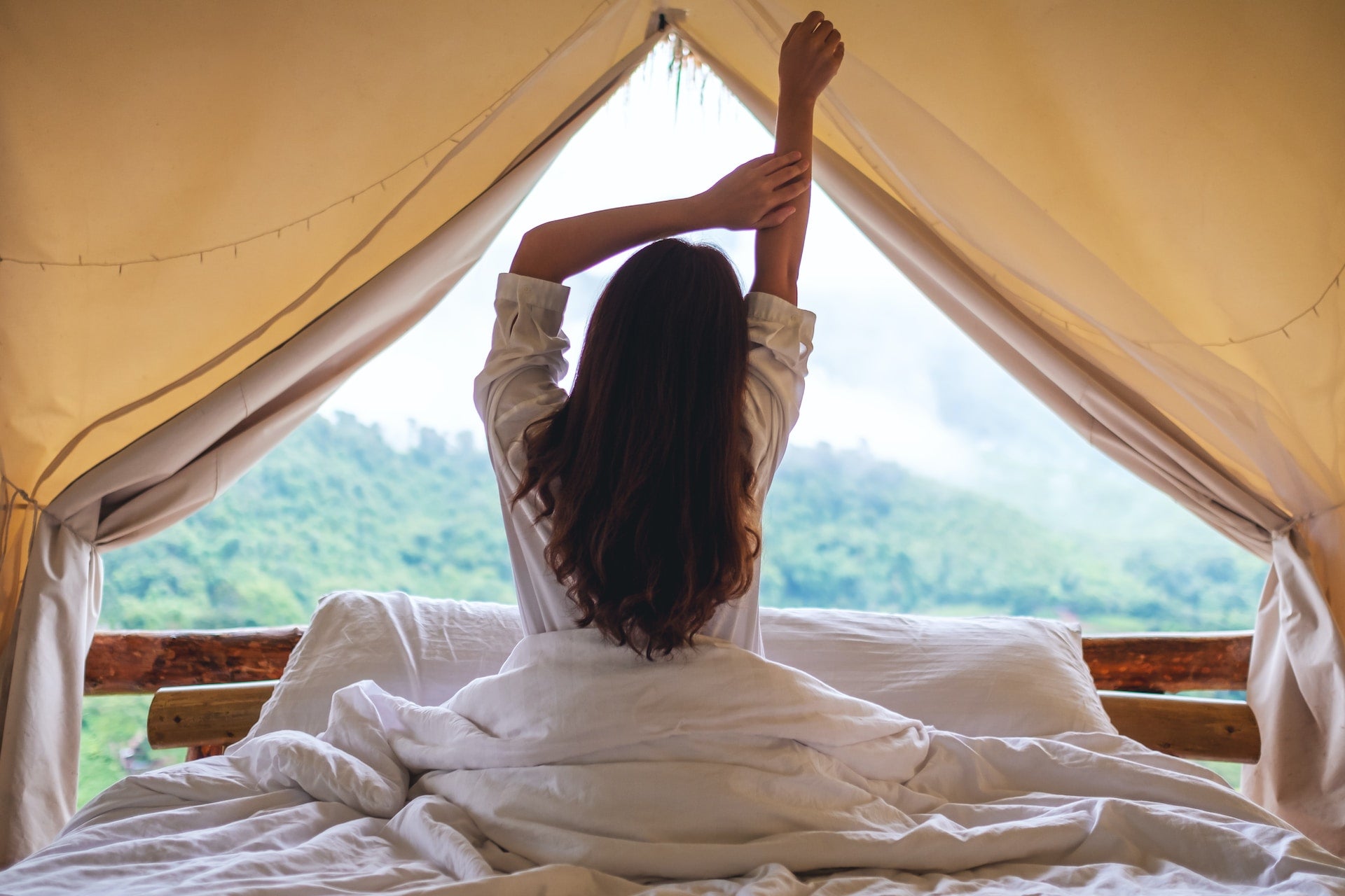 Woman stretching while sitting in bed in a tent overlooking a vista