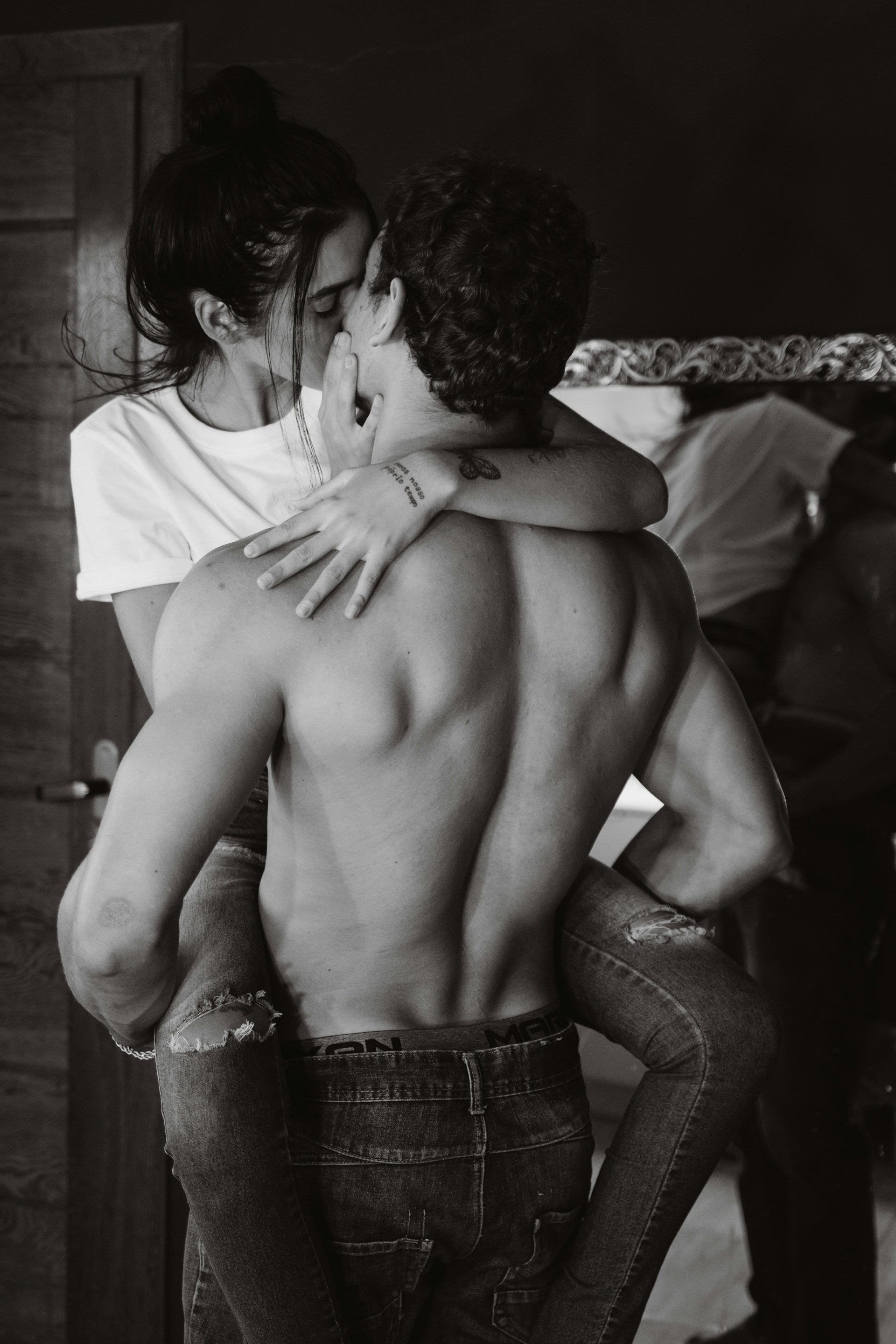 A young couple embracing each other while the man is shirtless wearing jeans and the girl has her hair in a messy bun