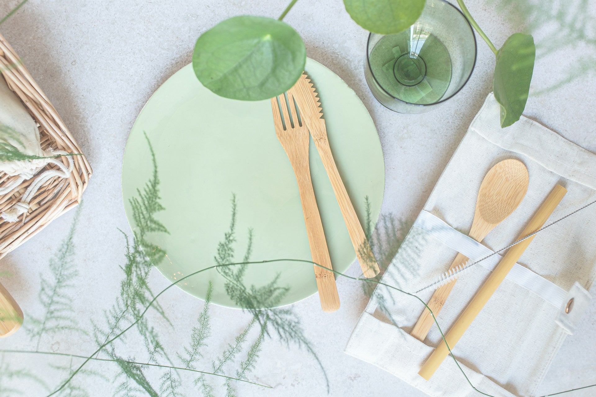A flatlay image of zero waste goods including bamboo cutlery set, cotton bags, and more; green theme
