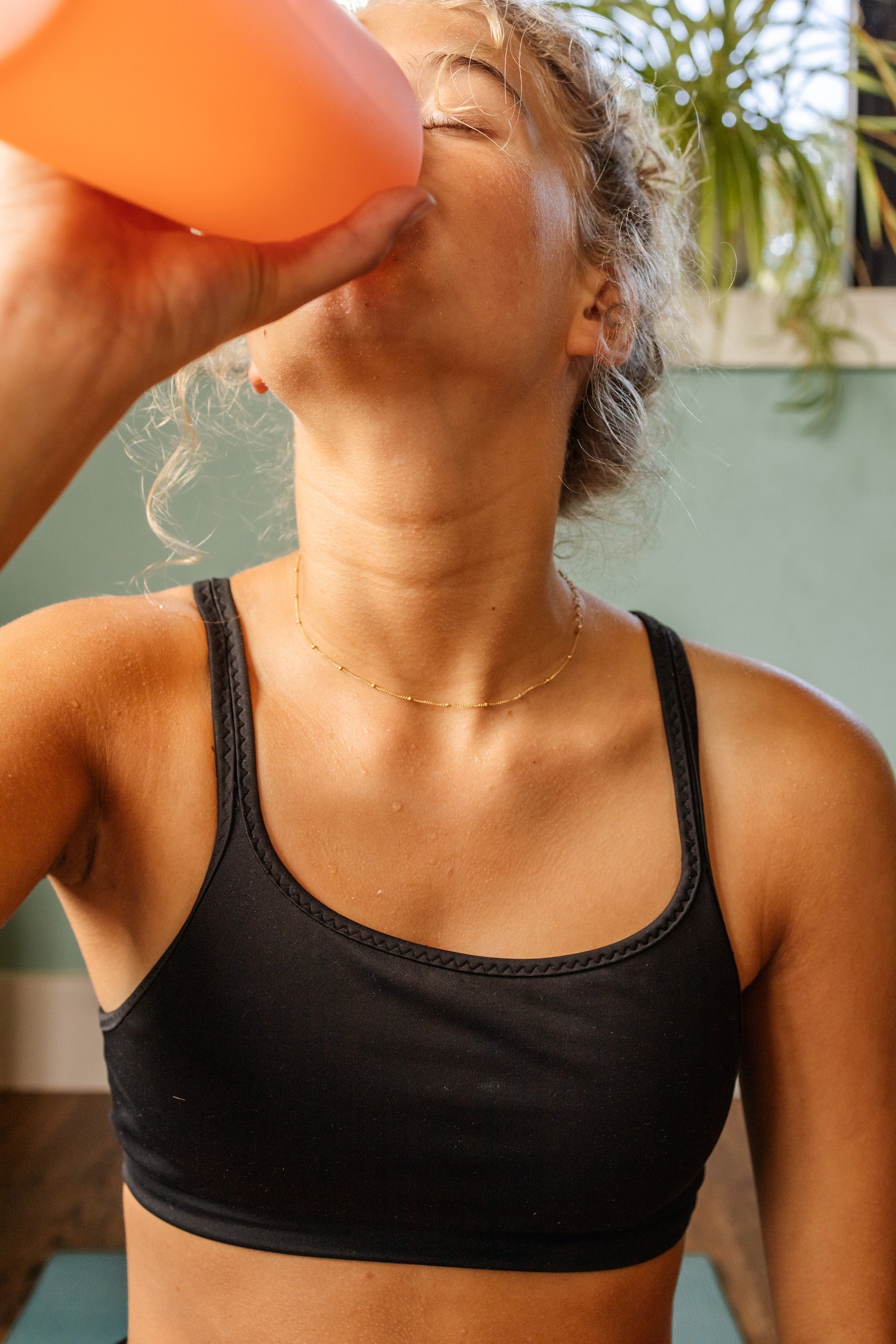 Blonde woman drinking water from an orange water bottle.