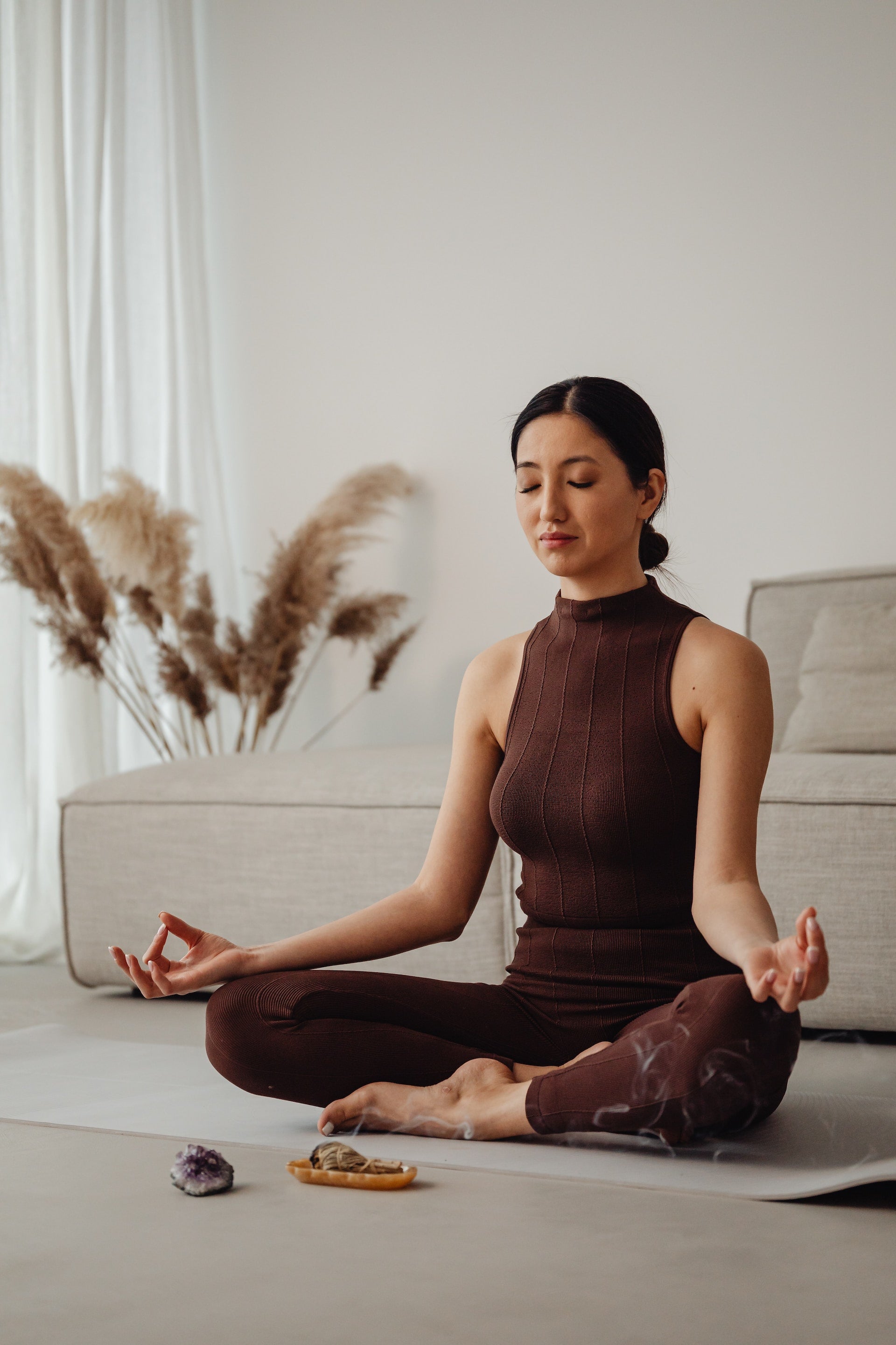 Dark-haired woman wearing a brown workout outfit meditating peacefully