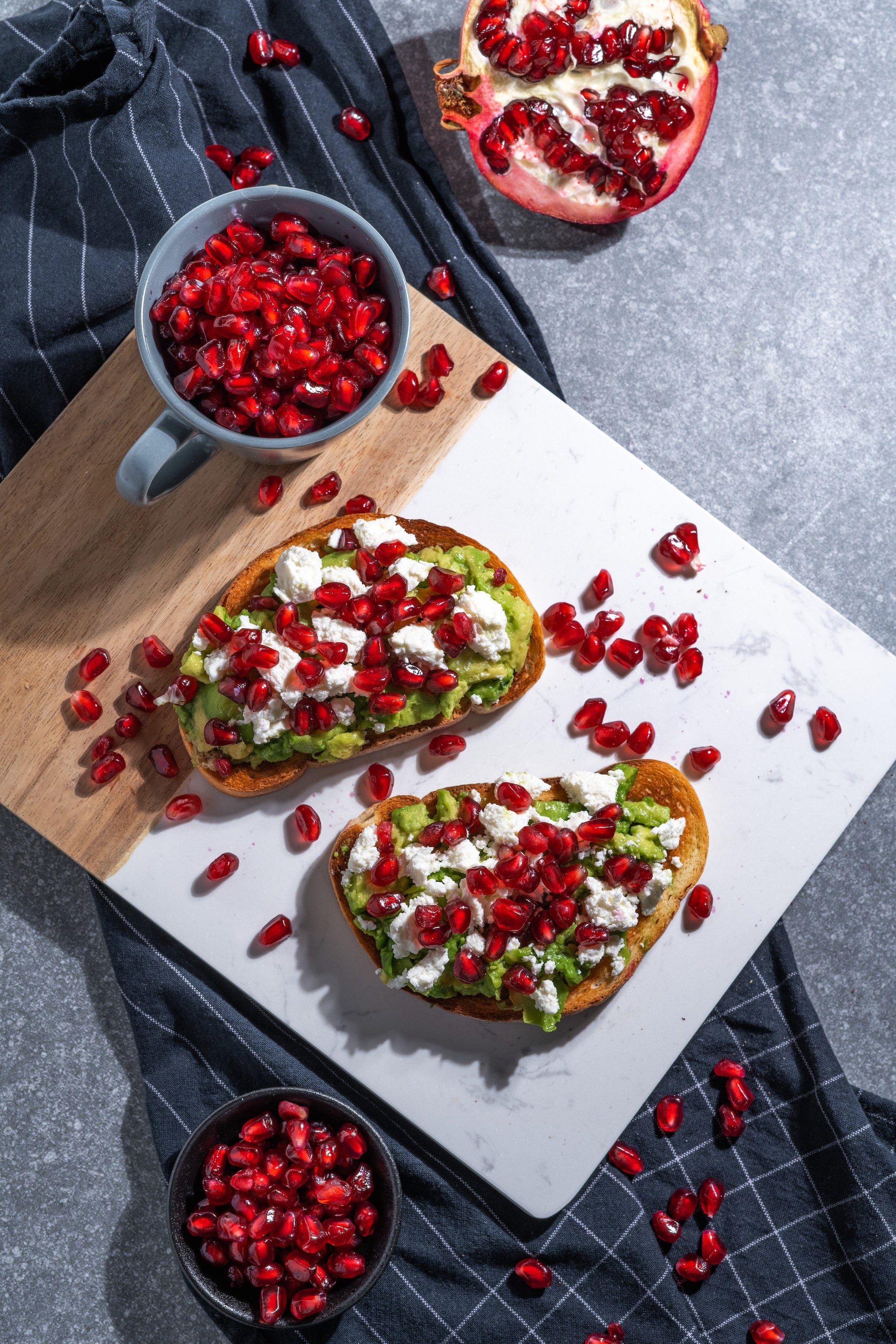 Avocado and pomegranate avocado toast on a cutting board laid out very aesthetically.