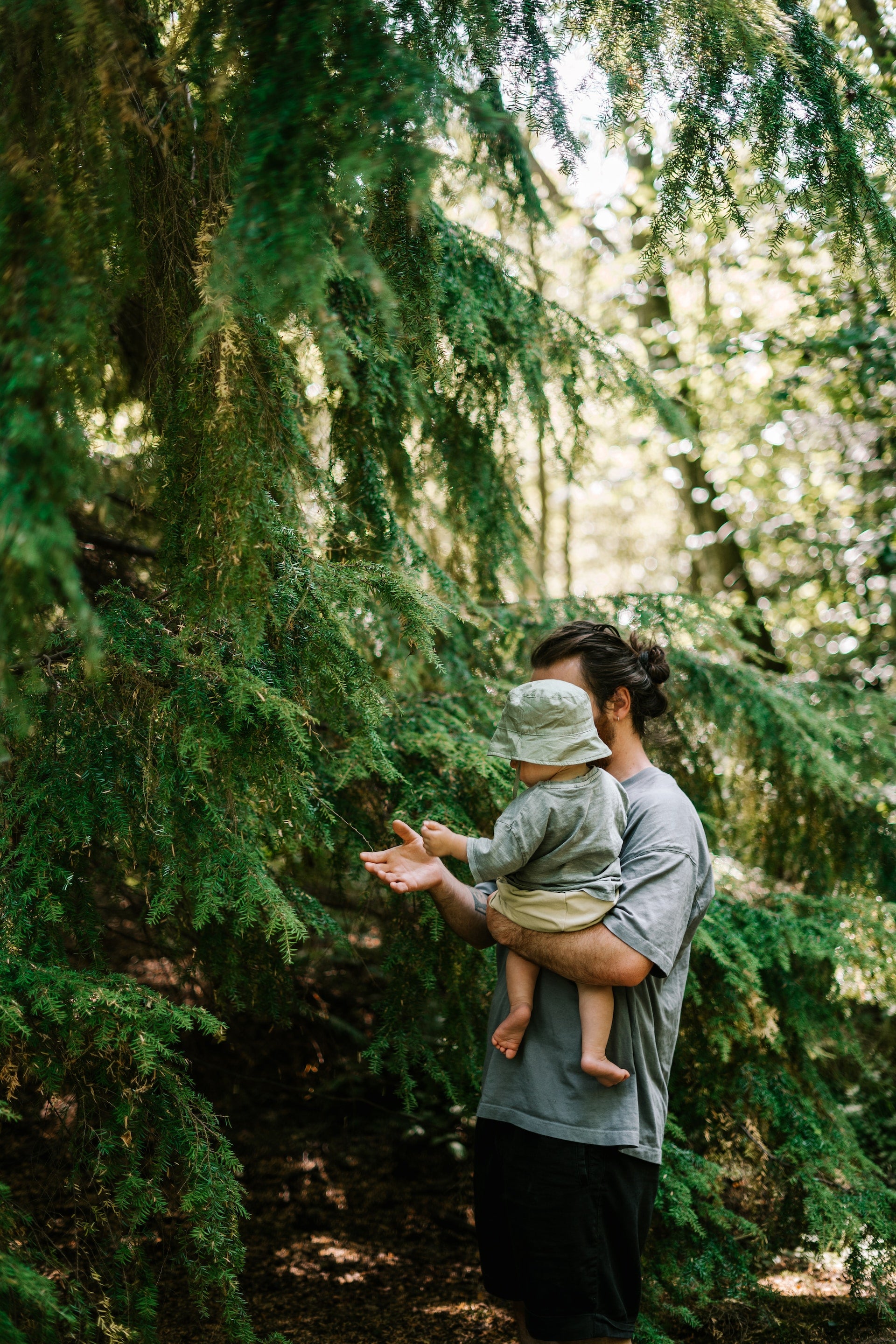 Man with long hair holding a baby while walking through the forest