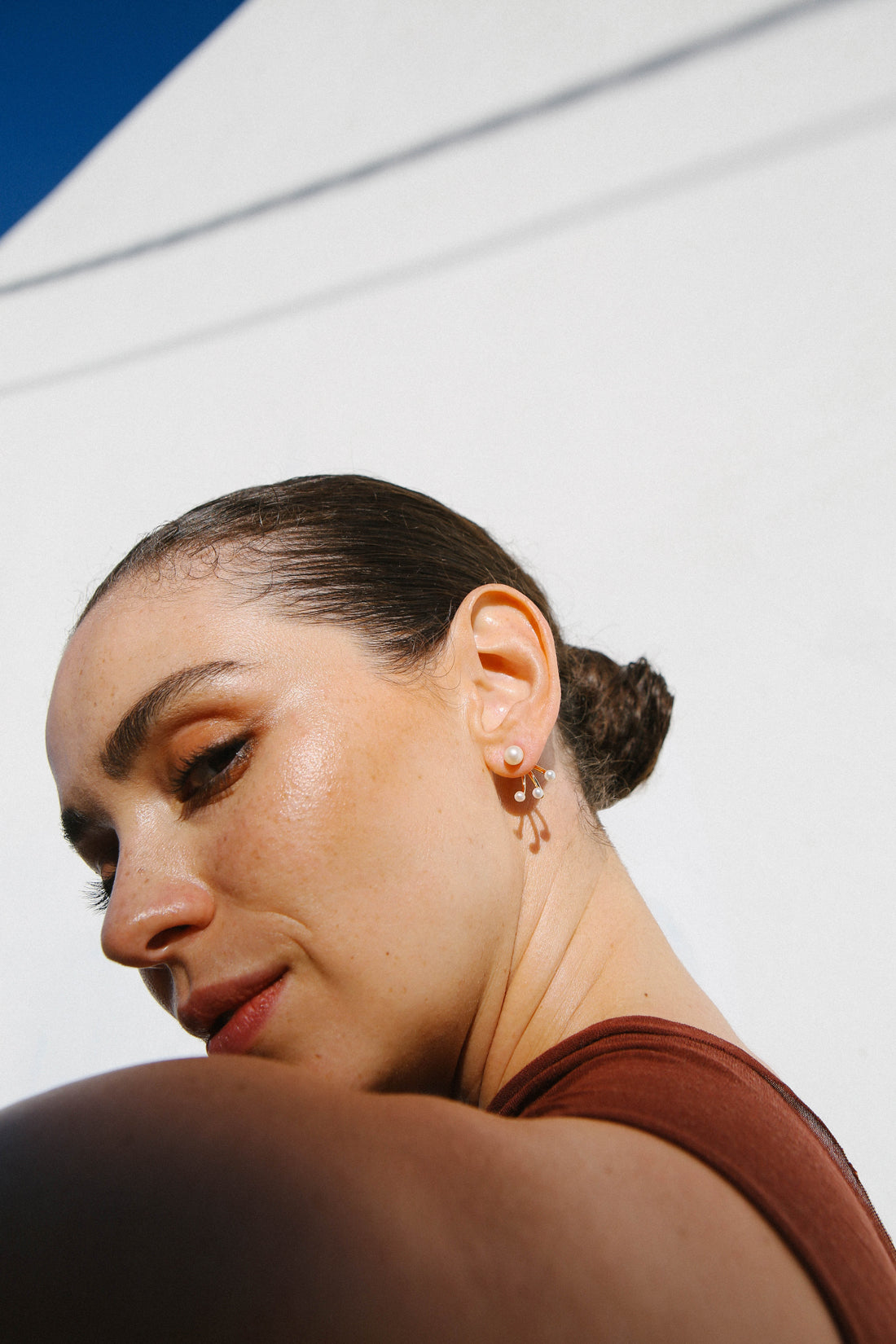 Model looks over her shoulder, and shows a single gold and pearl earring.