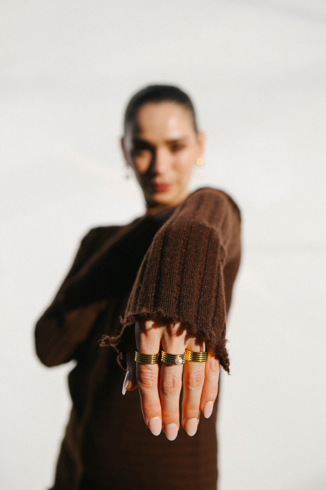 Model wears brown cardigan with arm held out, showcasing three gold rings.