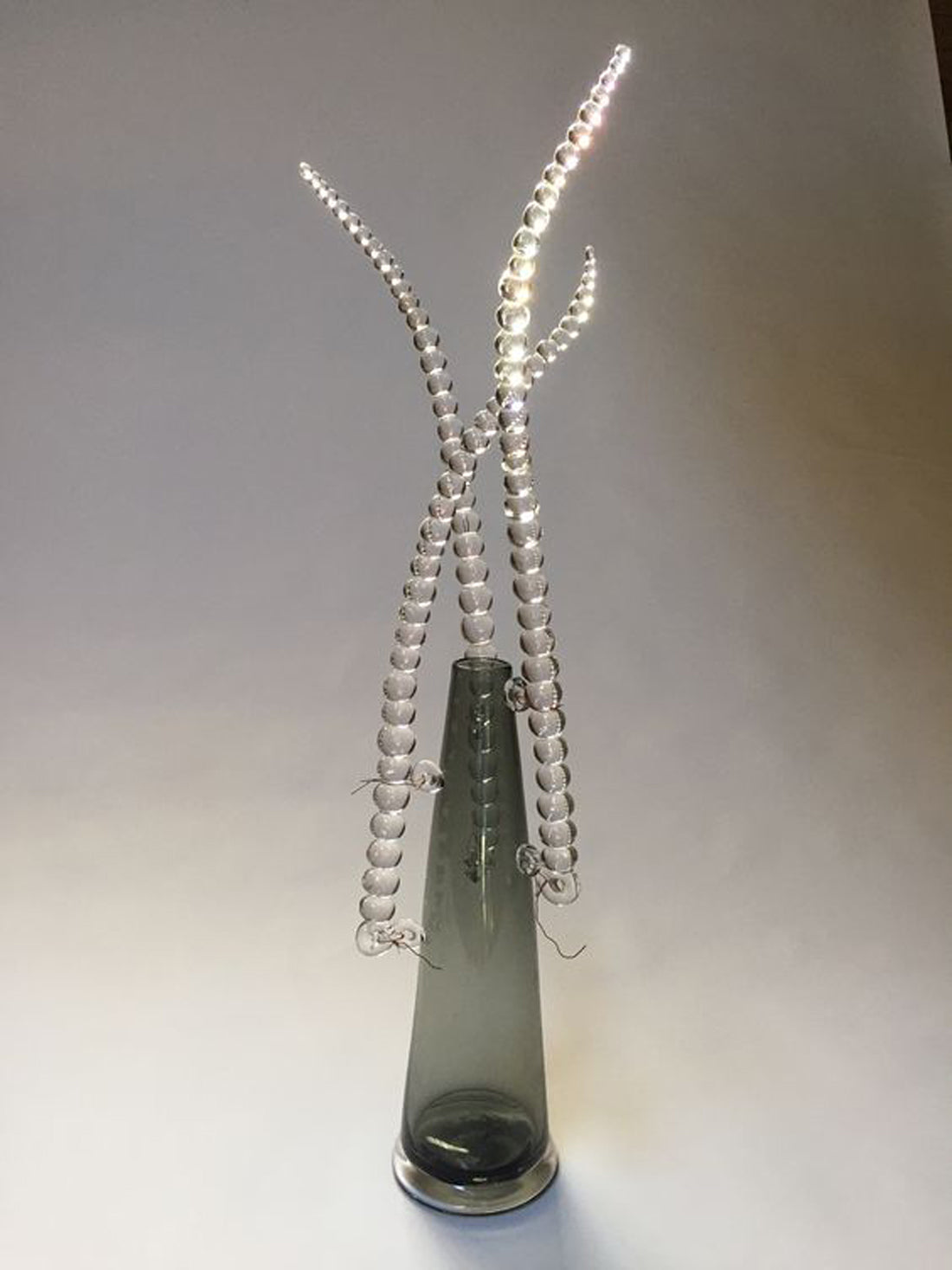 A green glass vase with three branches of clear glass beads.