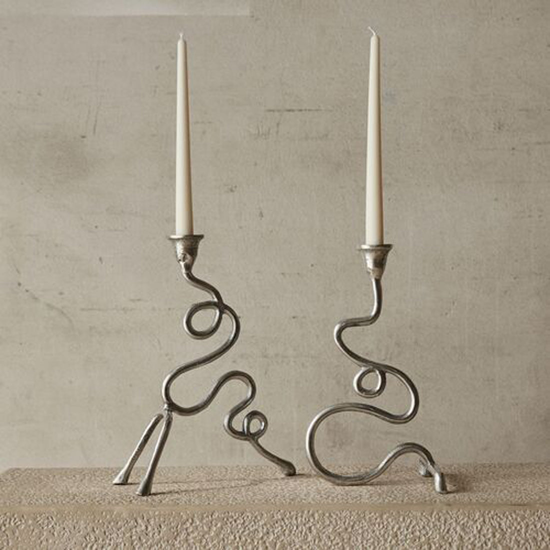 A pair of metal candelabras holding two white tall thin candles.