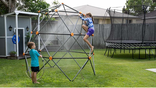 Two kids climbing on a climbing dome next to a Springfree Trampoline.